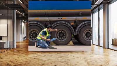 Asian truck drivers diligently inspecting the tires and wheels of their trucks for safety, ensuring secure and reliable journeys on the road. Wall mural