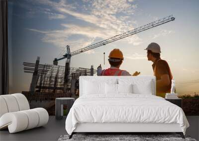 Asian two construction engineers supervising progress of construction project and crane background. Wall mural