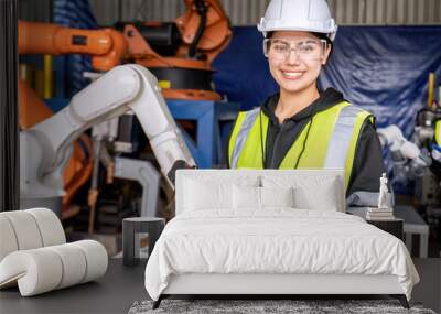 Young female asian service engineer holding robot controller operate robot arm automation factory Wall mural