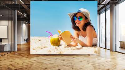 Lifestyle young asian woman relax and reading a book at the beautiful beach on holiday summer, blue sky background. Summer Concept. Wall mural