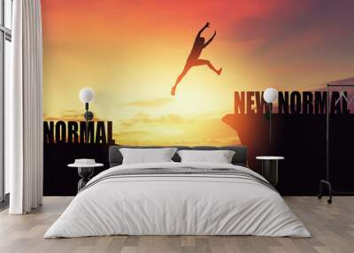 Silhouette man jumping between cliff with new normal word at tropical sunset beach. Freedom challenge and travel adventure holiday concept. Wall mural