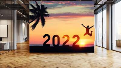 Silhouette man jumping with number like 2022 and palm tree at tropical beach on sunset sky abstract background. Happy new year and holiday celebration concept. Wall mural