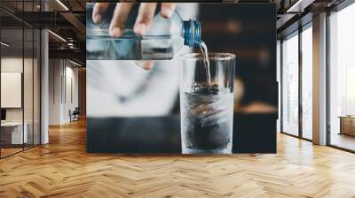 Woman hand pouring bottle of water to glass at cafe. Wall mural