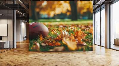 A brown football sits on a grassy field with fall leaves. Wall mural