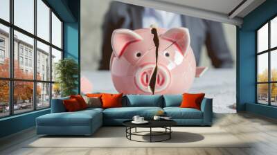 A broken pink piggy bank with coins scattered around symbolizes financial troubles, savings loss, or economic challenges in front of a blurred background. Wall mural