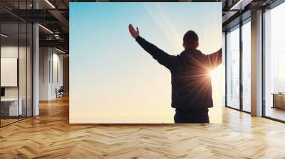 A person stands in silhouette against a vibrant sunset, arms raised in joy and freedom, embracing the beauty of nature. Wall mural