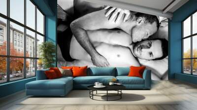 Attractive male gay couple lying together in bed, one kissing other looking at camera Wall mural