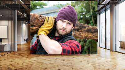 Handsome male lumberjack carries wood log on his shoulder Wall mural