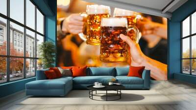 A group of friends holding beer mugs and glasses cheering and toasting together at a lively gathering in a bar or pub setting Wall mural