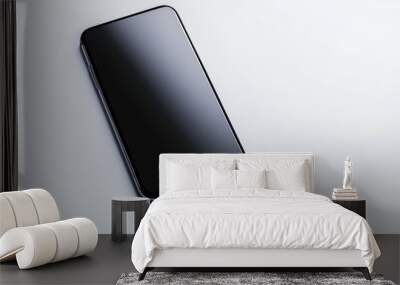 A black cell phone is laying on a white surface Wall mural