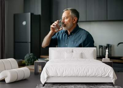 A man is drinking water while sitting at a table with a bowl of broccoli Wall mural