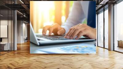 A man is typing on a laptop in front of a paper with graphs Wall mural