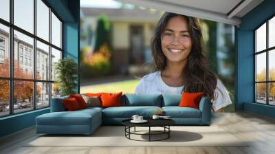 A woman with long brown hair is smiling and standing in front of a house Wall mural