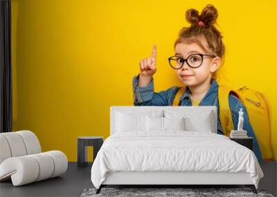 A young girl wearing glasses and a yellow jacket is pointing to the sky Wall mural