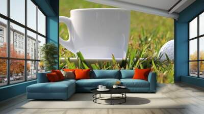 White cup of coffee next to a golf ball, on a green lawn Wall mural