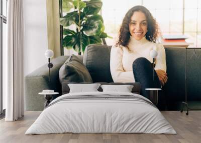 Latin woman smiling and sitting on sofa Wall mural