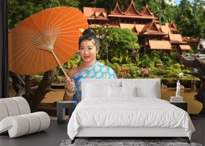 Beautiful Asian woman in Thai National costume holds a paper umbrella posing for photos at a Thai house. Wall mural