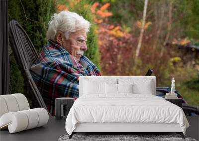 Senior man sitting in the rocking chair reading text message on smartphone. Mature man using his smartphone on the veranda. Portrait of a retired man reading a message on his cellular. Wall mural