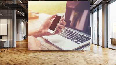 young business man hand holding phone and using laptop computer Wall mural