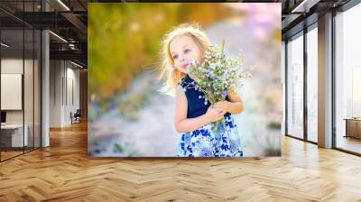 lovely cute little girl with blond hair walks outdoors at sunset, holds a bouquet of wildflowers in her hands, happy childhood Wall mural