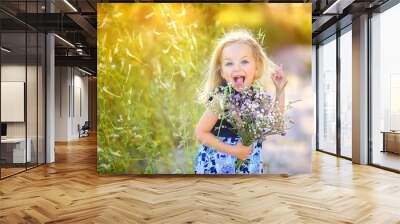 playful cute little girl playing outdoors at sunset, holding a bouquet of wildflowers and having fun, happy childhood Wall mural