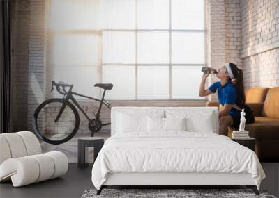 Asian woman cyclist. She is exercising in the house. By cycling on the trainer And play online bike games She breaks to drink water Wall mural