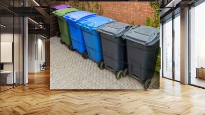 Plastic Waste Recycling Wheelie Bins lined up and secured in a UK garden storage area beside house brick wall, waiting for weekly council collection Wall mural