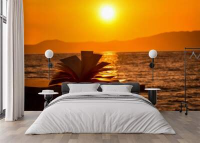 Silhouette of an open book during sunset at the beach by the sea. Sunset summer reading Wall mural