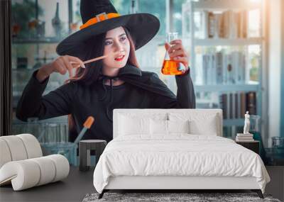 Attractive beautiful Asian woman dressed as a witch using magic wand casting spell to potion in test tube at modern laboratory, Halloween holidays.   Wall mural