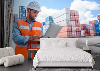 Confident man engineer wearing white safety helmet using computer laptop and check for control loading containers box from Cargo freight ship for import and export, transport Wall mural