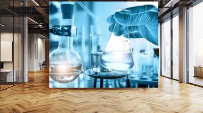 hand of scientist holding flask with lab glassware in chemical laboratory background, science laboratory research and development concept   Wall mural