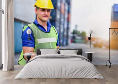 Young confident Caucasian man engineer using digital tablet and wearing yellow safety helmet and check for control loading containers box from Cargo freight ship for import and export, transport. Wall mural