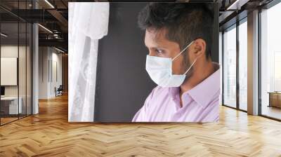 A young asian man with protective mask in face looking through window  Wall mural