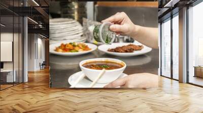 A Chinese restaurant waitress garnishing a soup with chives in a white bowl to bring to a table Wall mural