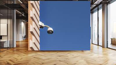 A surveillance camera placed in a corner of a building on a day with the sky completely free of clouds Wall mural