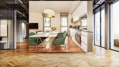 Dining room of a house with open kitchen, marble table with gold metal legs, smooth white furniture and stainless steel appliances Wall mural