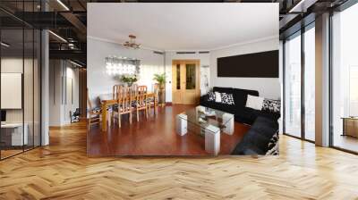 Living room of a residential home with a wooden dining table with matching chairs, a corner sofa covering two walls upholstered in black fabric and reddish stoneware floors Wall mural