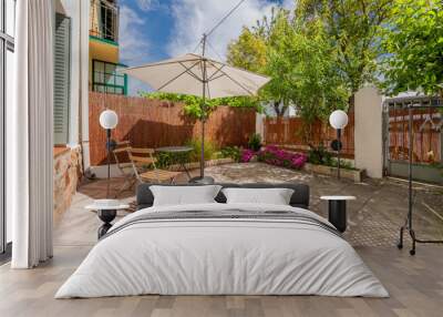 Terrace of a single-family home with tiled floor, folding metal table and chairs under a parasol and plants in pots Wall mural