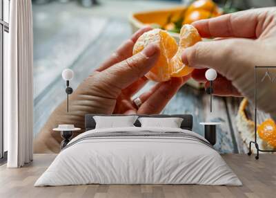 two man's hands separating a segment of ripe tangerine and in the background a basket Wall mural