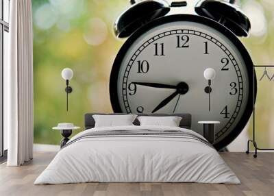 vintage alarm clock show before 8 o'clock on the table with green leafs blurred background and copy space. Wall mural