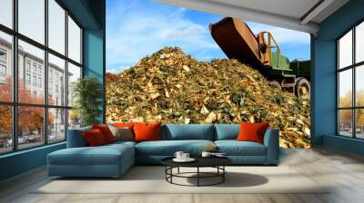 A large pile of organic waste, primarily corn husks, is being processed by a machine in an outdoor setting with a blue sky. Wall mural