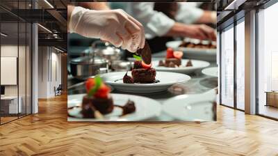 A photo of a chef carefully placing a chocolate garnish on top of a rich mousse dessert, with other plated desserts in the background. Wall mural