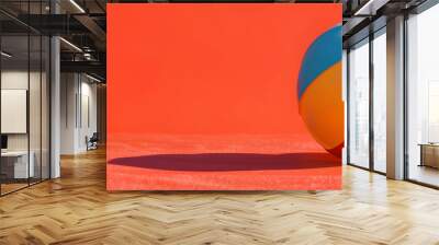 A red and yellow beach ball is sitting on a red surface. The ball is the main focus of the image, and it is a simple, playful scene. The bright colors of the ball Wall mural