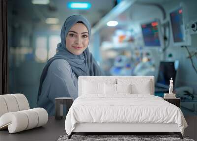 Confident female doctor wearing hijab smiles at camera in hospital ward in front of medical equipment, including monitors, laptops professional environment in modern Middle East healthcare facility. Wall mural