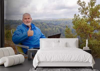 Mature male tourist is working on a laptop on top of the High Mountain. Wall mural