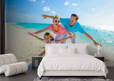 Family at the beach, mother, father and daughter playing on the sand dressed in colorful tropical outfits Wall mural