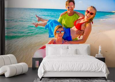 Happy family at the beach, mother, father and daughter with pink lifesaver standing on the beach  Wall mural