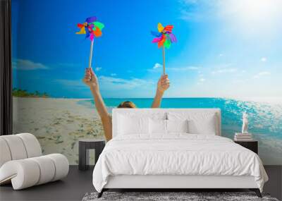 Young girl at the beach, playing with windmill, pinwheel on the sand, dressed in colorful tropical outfit Wall mural