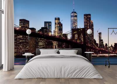 Beautiful Brooklyn Bridge and the illuminated Manhattan's skyline at dusk with dark blue sky and smooth water surface. Picture taken from the Brooklyn district, New York, USA. Wall mural