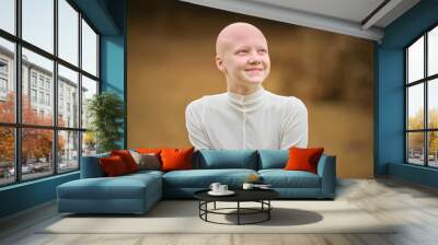 Portrait of young happy hairless girl with alopecia in white cloth on autumn park background, radiant smile of bald pretty teenage girl symbolizing joy acceptance individuality and her unique beauty Wall mural